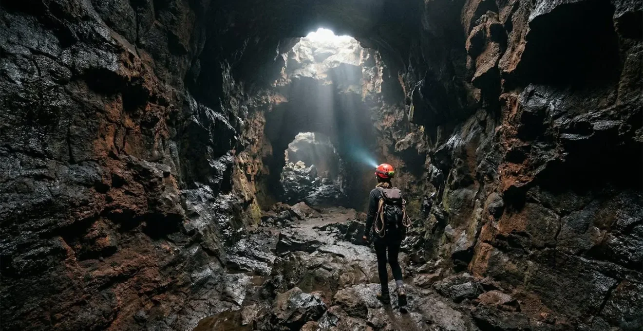 Explorateur progressant dans un tunnel de lave à La Réunion avec un puits de lumière naturelle illuminant les parois volcaniques