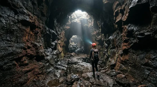 Explorateur progressant dans un tunnel de lave à La Réunion avec un puits de lumière naturelle illuminant les parois volcaniques