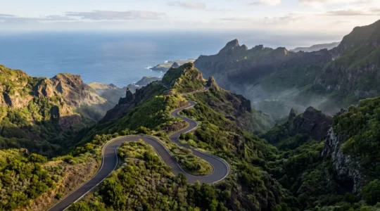 Vue aérienne spectaculaire d'une route sinueuse serpentant à travers les paysages montagneux volcaniques de La Réunion avec l'océan en arrière-plan
