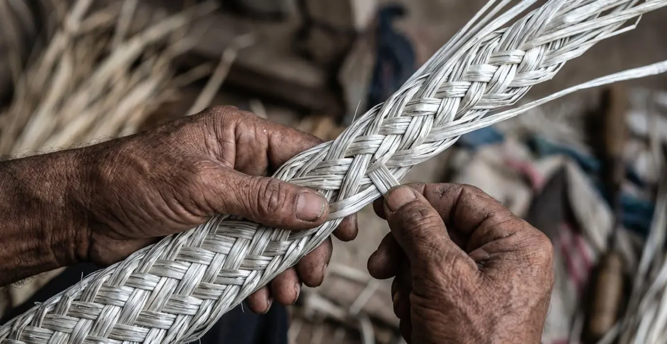 Mains d'artisane tressant délicatement des fibres de paille de chouchou séchées pour créer un chapeau traditionnel